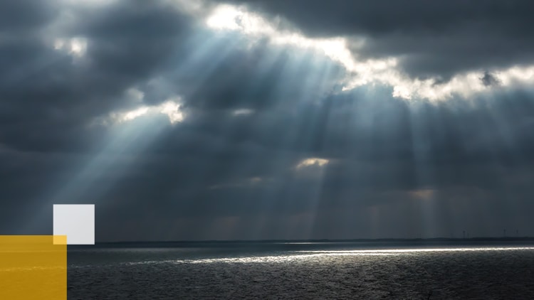 Sun rays shining through clouds over an ocean.