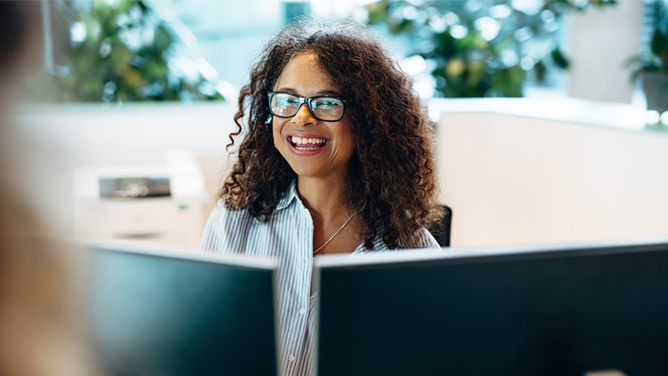 Woman looking at someone from over the top of a computer monitor